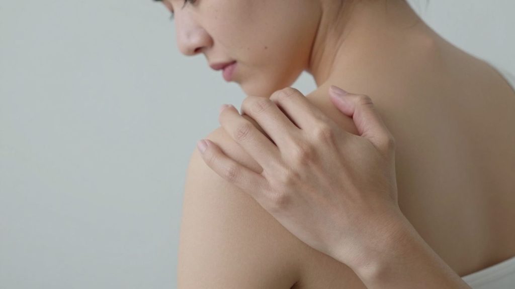 Woman touching sore shoulder area showing signs of shoulder pain when lifting arm 