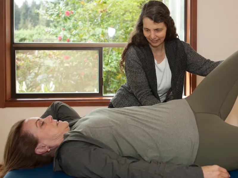 Laura Yedwab working with a client as she lies on a low padded table