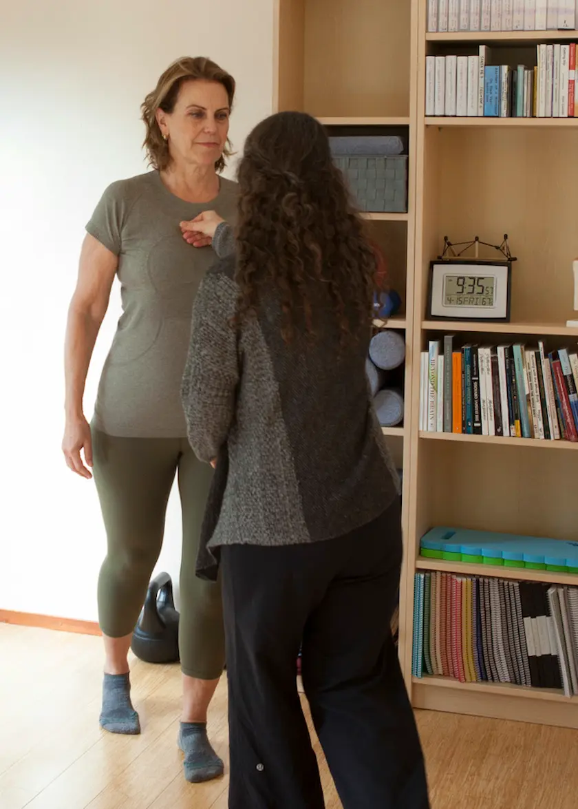 Laura Yedwab walking beside a fully clothed client in her studio, one hand resting on the client&rsquo;s sternum as the client takes a step.